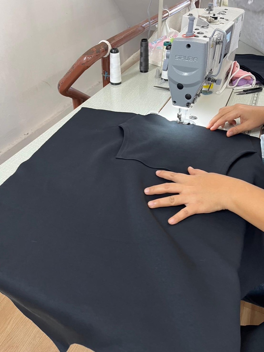 Close-up of a seamstress hand-sewing an ENYOUGH hoodie on an industrial machine in Bangkok